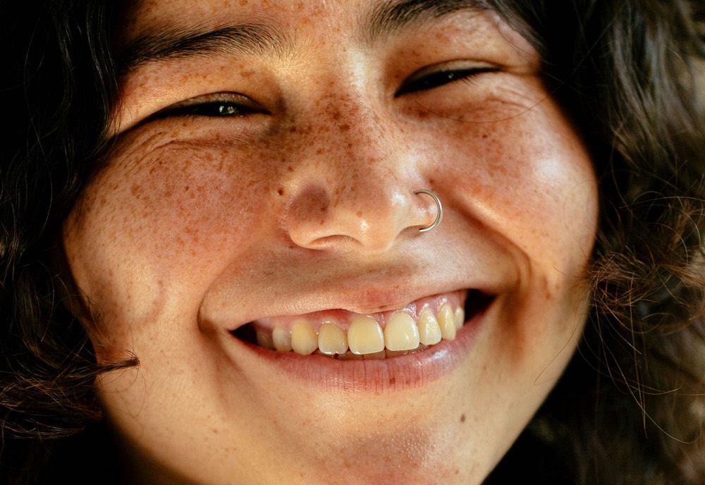 A close-up of a woman smiling warmly, freckles across her face.