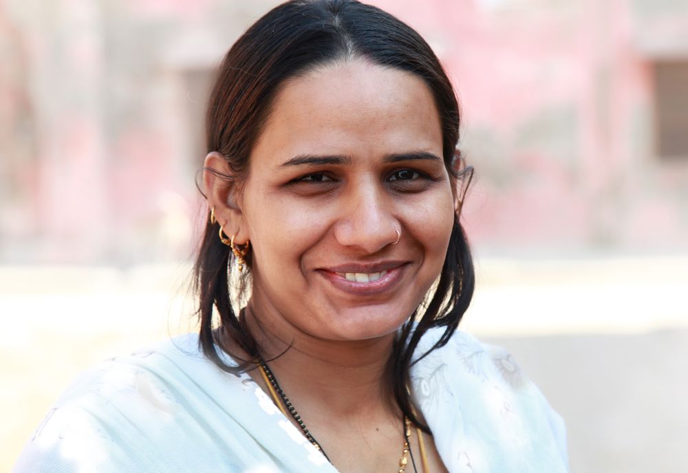 A smiling woman with dark hair and a white scarf, outdoors.