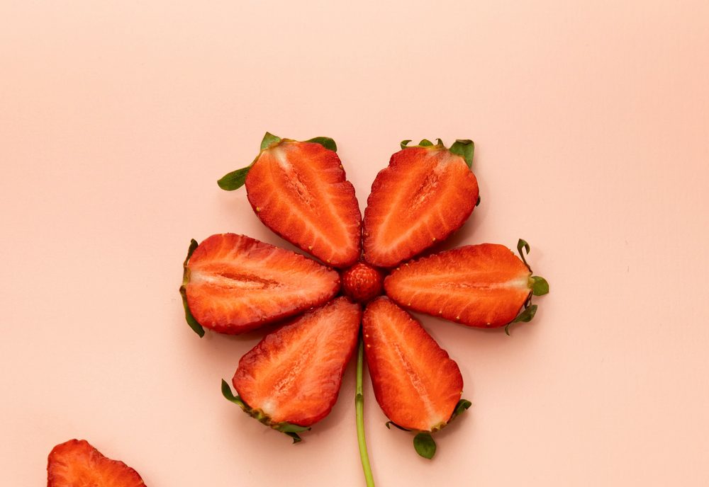 Sliced strawberries arranged as a flower on a soft peach background.